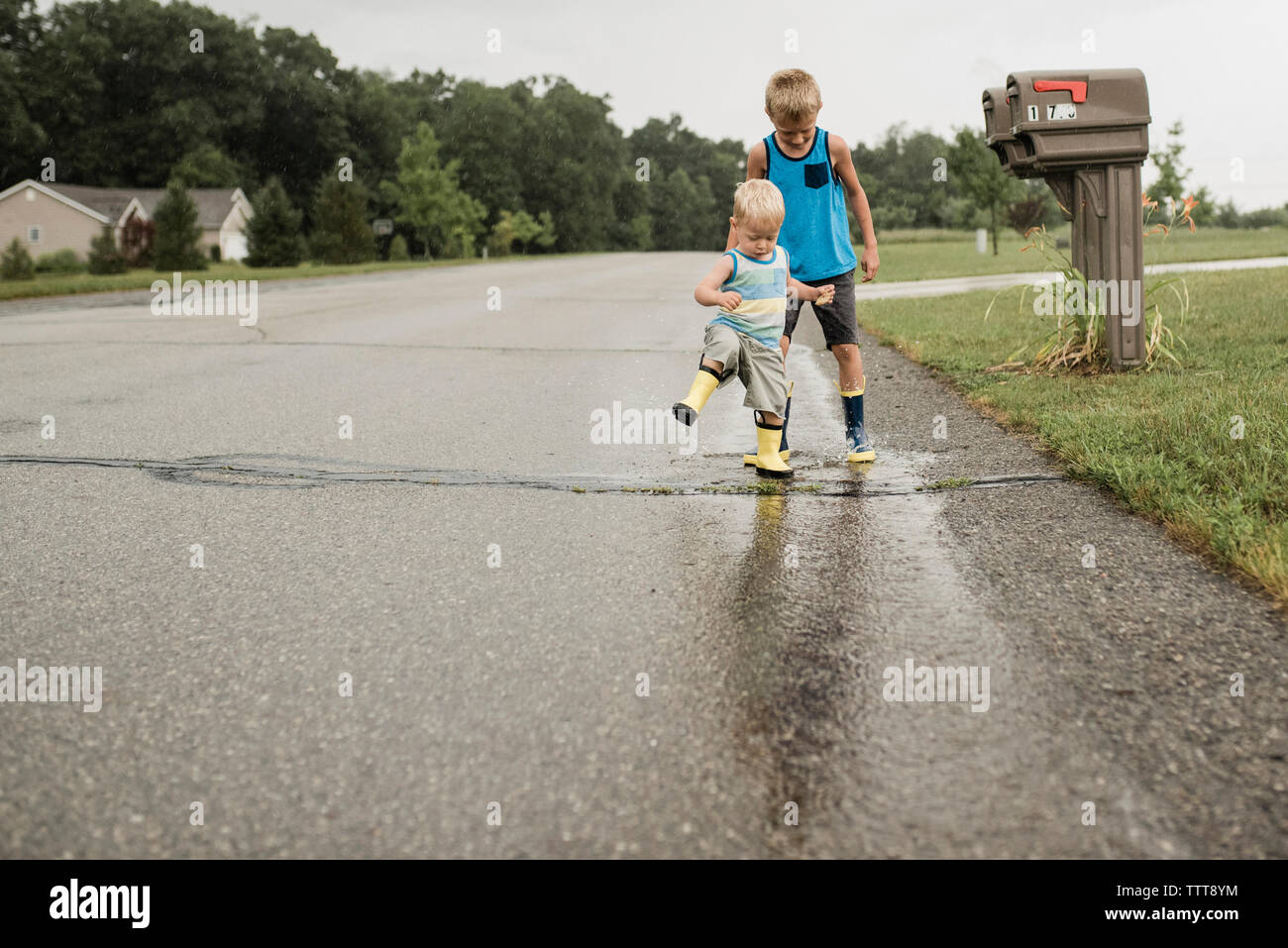 Full length of playful brothers stamping feet in puddle on road during monsoon Stock Photo