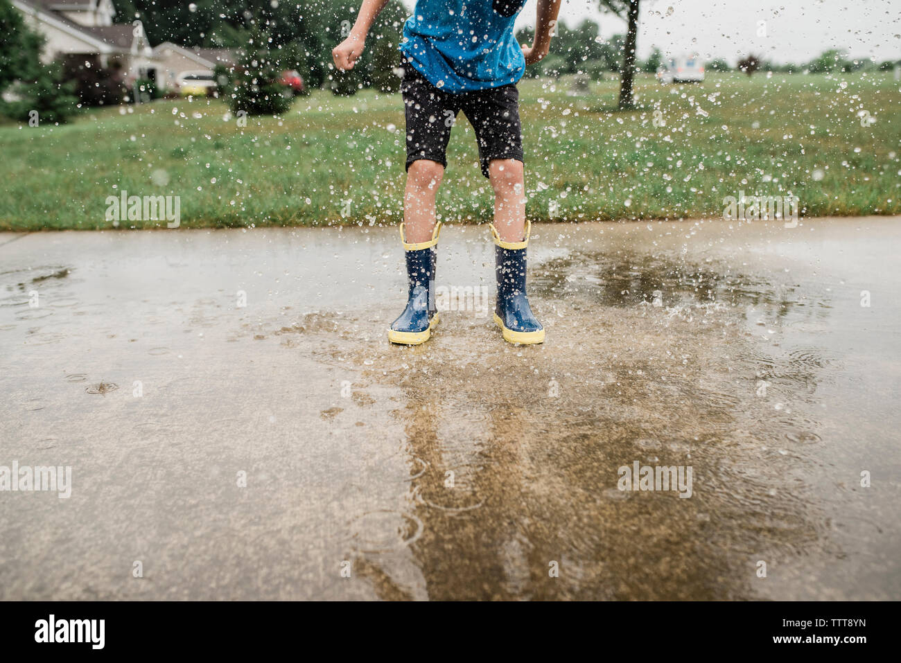 Low section of playful boy stamping feet in puddle on road during monsoon Stock Photo