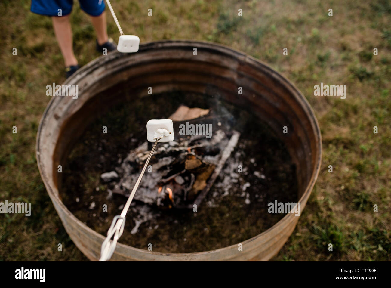 Low section of boy roasting marshmallow in skewer over fire pit at backyard Stock Photo