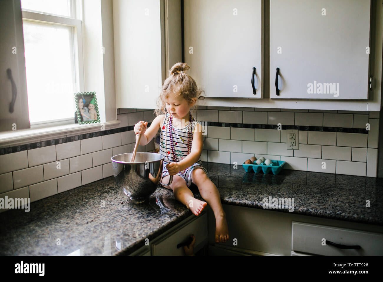 Girl preparing food in container while sitting on kitchen counter at home Stock Photo