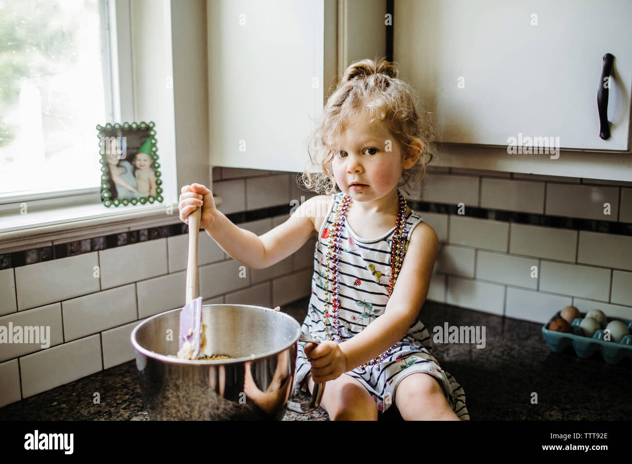 Portrait of cute girl preparing food in container while sitting on kitchen counter at home Stock Photo