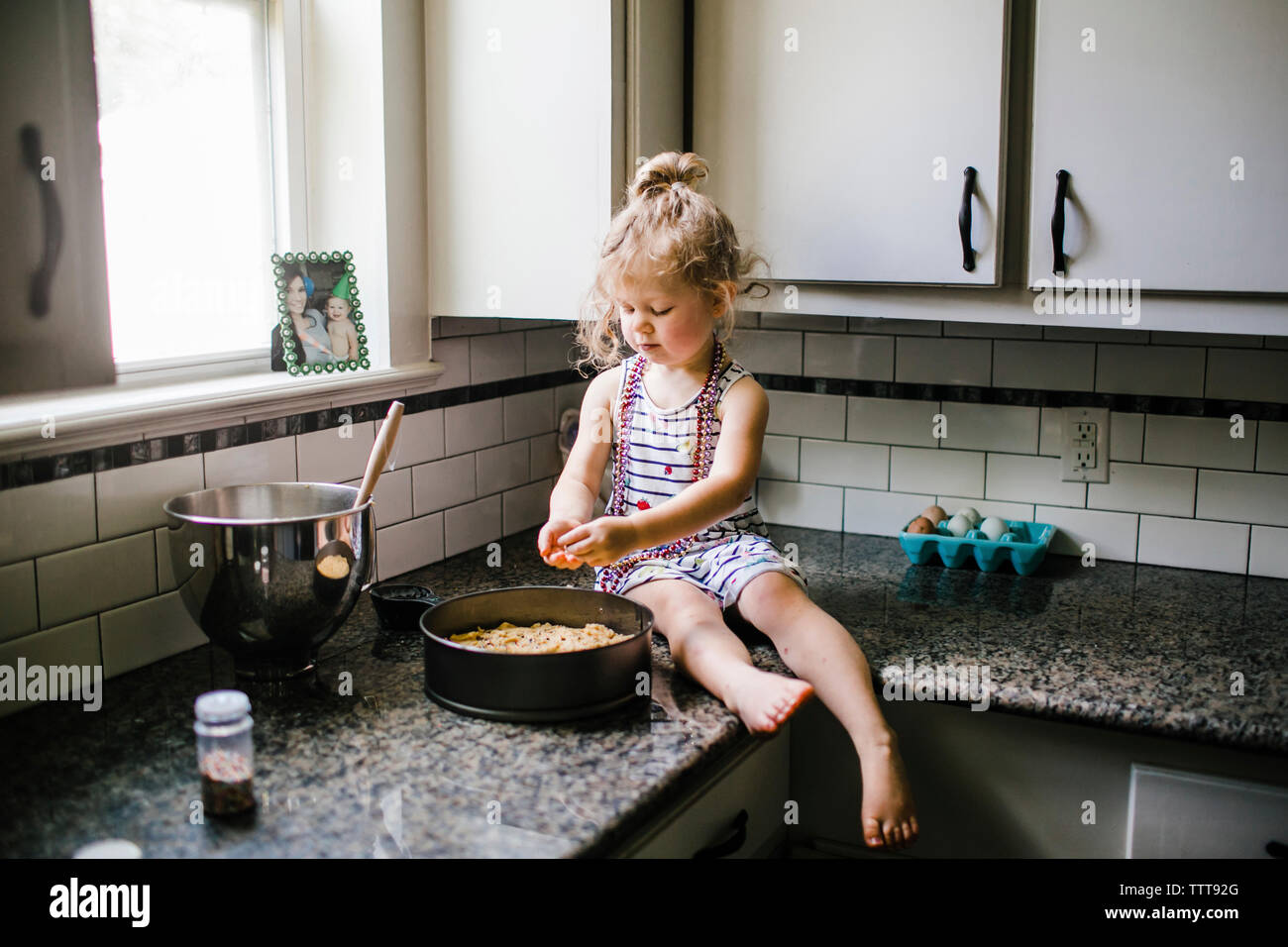 Girl preparing food in container while sitting on kitchen counter Stock Photo
