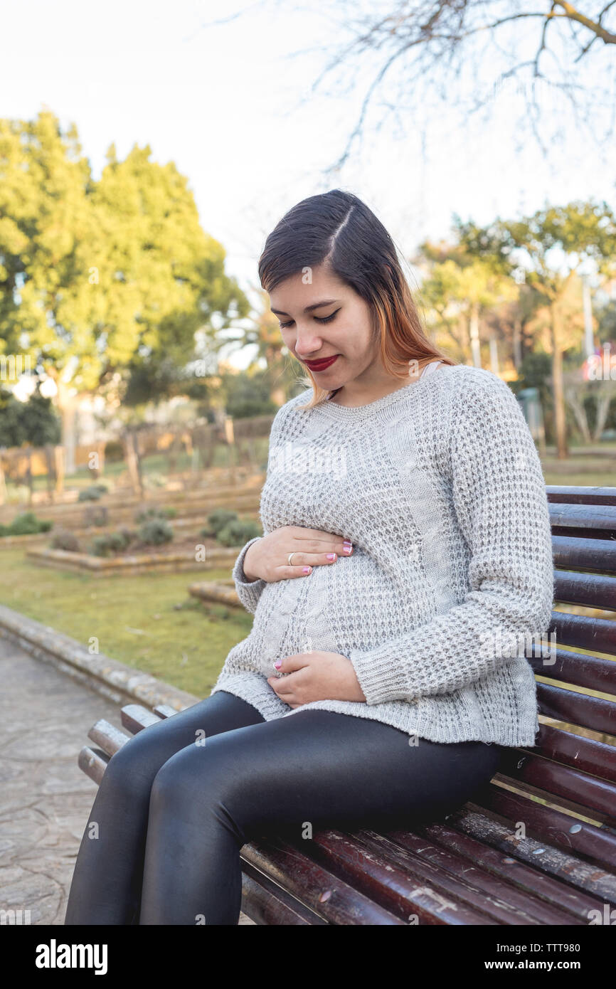 Portrait of a young pregnant woman sitting in the park holding belly Stock Photo