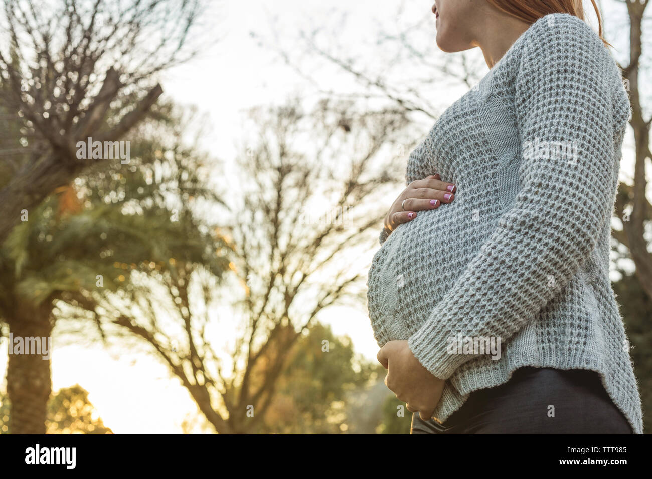 Young pregnant woman holding her belly with sunset behind her Stock Photo