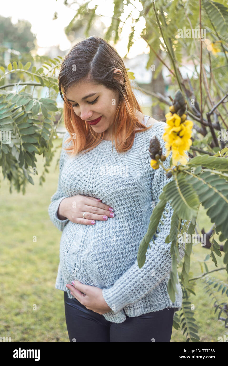 Portrait of a young pregnant woman holding her belly between flowers Stock Photo