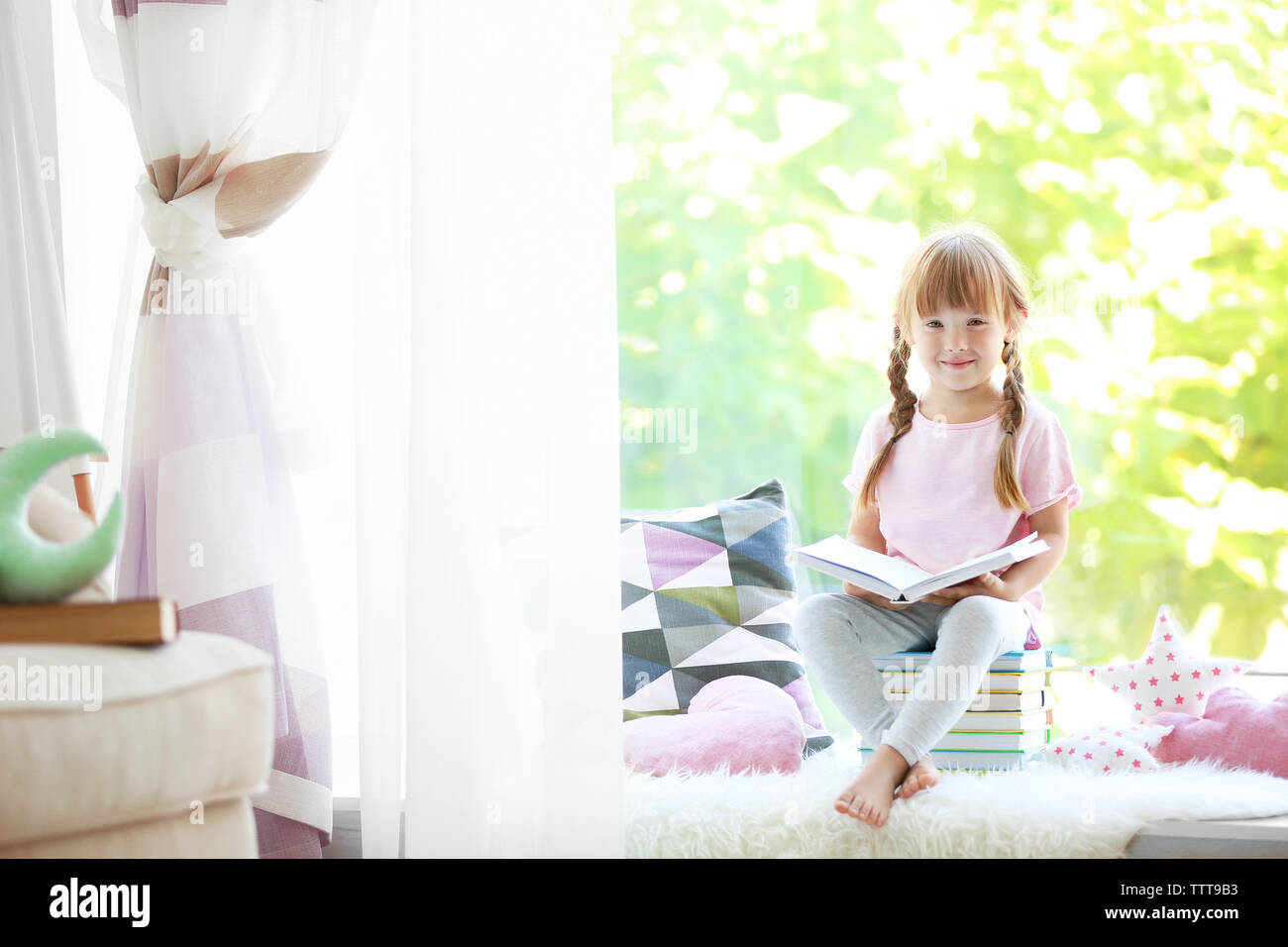 Beautiful little girl sitting on pile of books near window Stock Photo ...