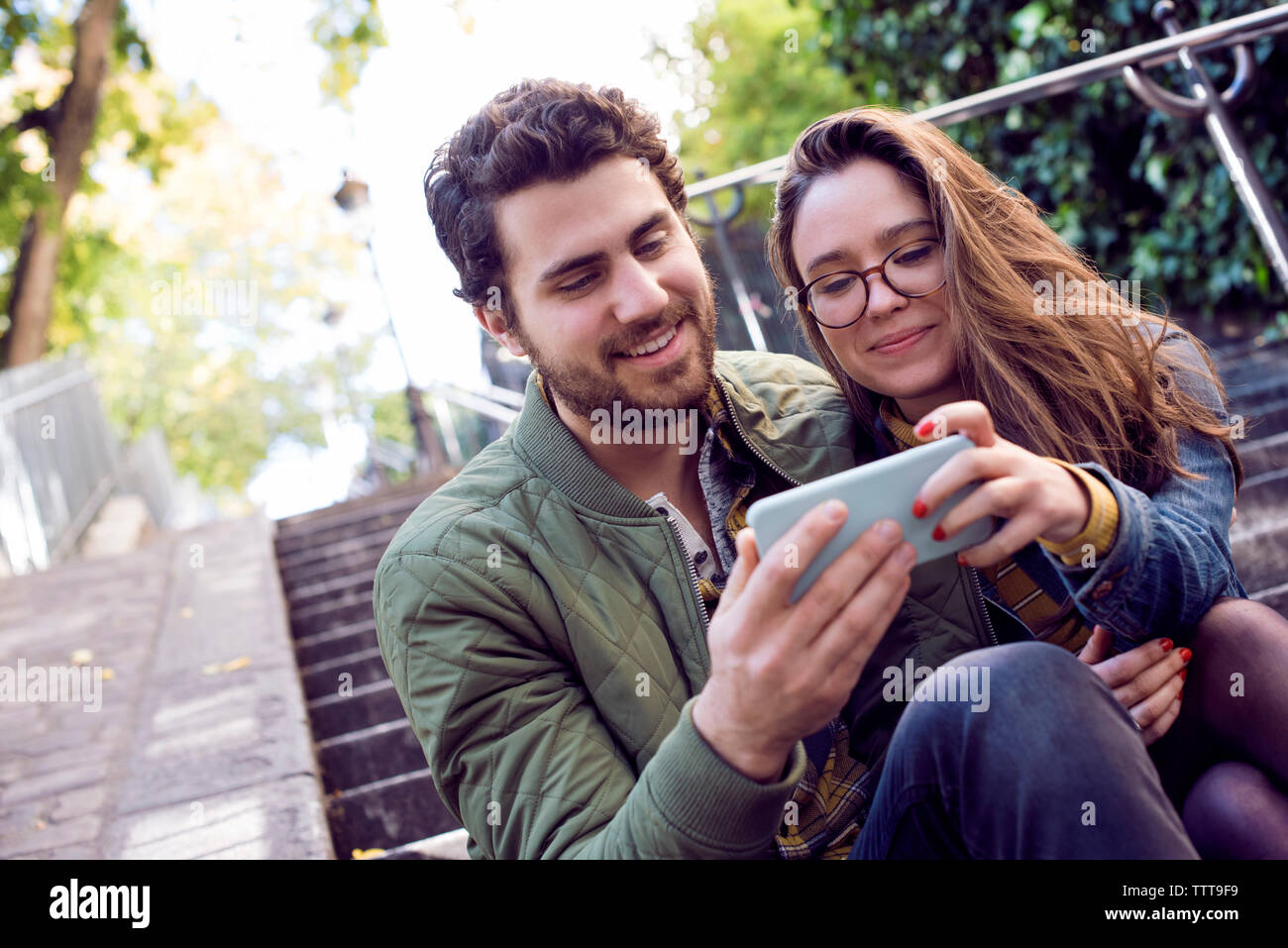 Happy young couple using smart phone while sitting on steps Stock Photo