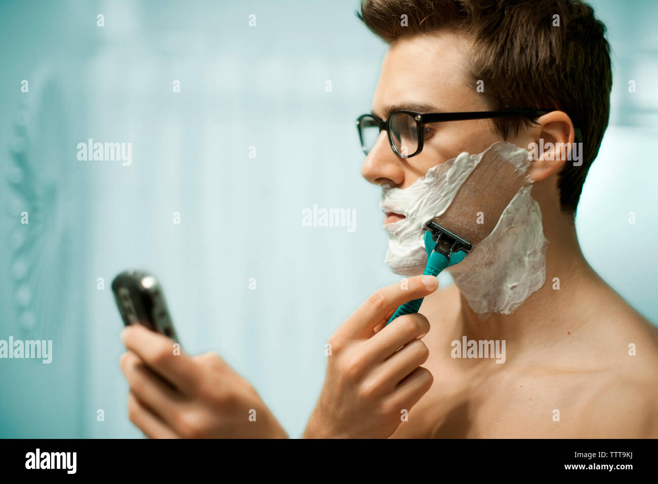Man using phone while shaving face at home Stock Photo