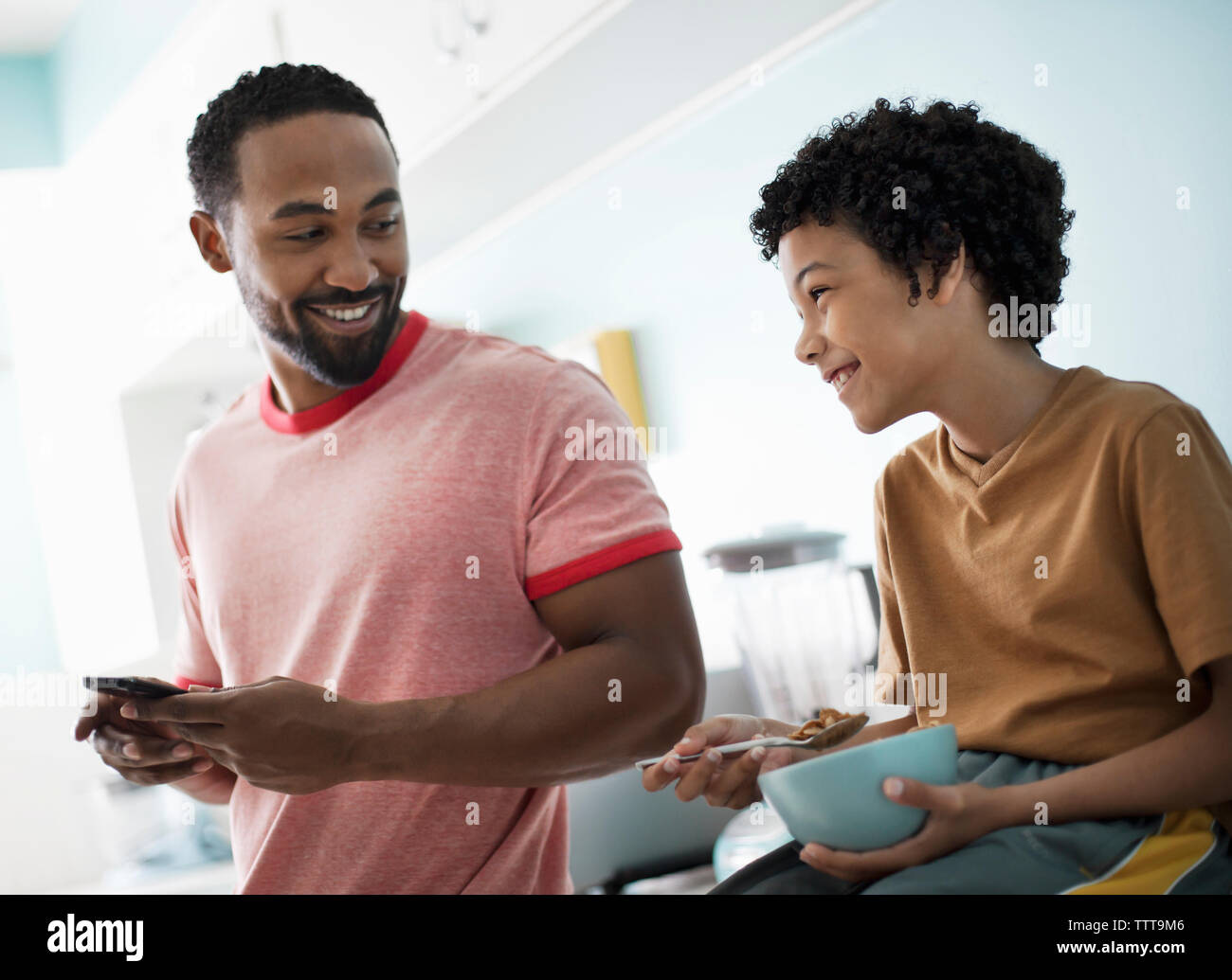 Father using mobile phone while son having breakfast at kitchen counter Stock Photo