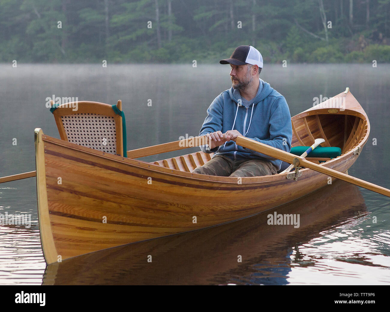 Man looking away while rowing boat on lake against trees during sunset Stock Photo