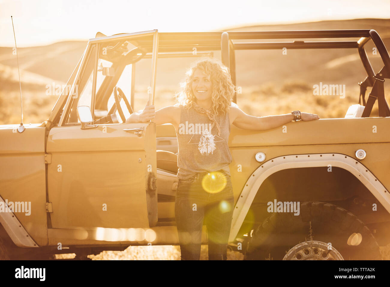 Cheerful woman looking away while standing against off-road vehicle during sunny day Stock Photo