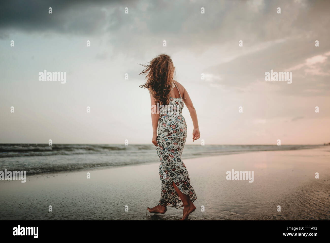 Rear view of woman walking at beach against sky during sunset Stock Photo