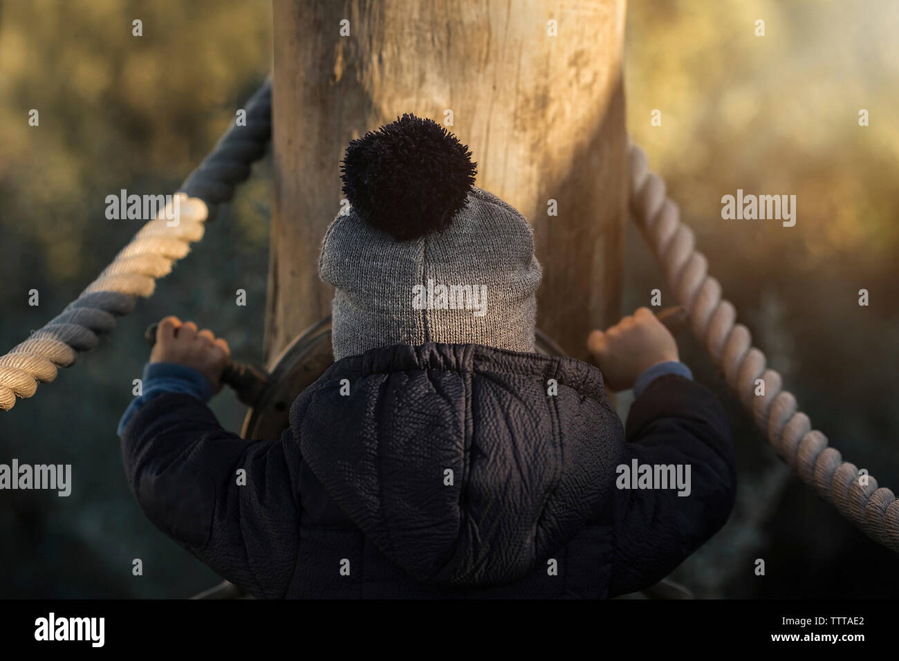 Rear view of boy in warm clothing spinning steering wheel at playground Stock Photo