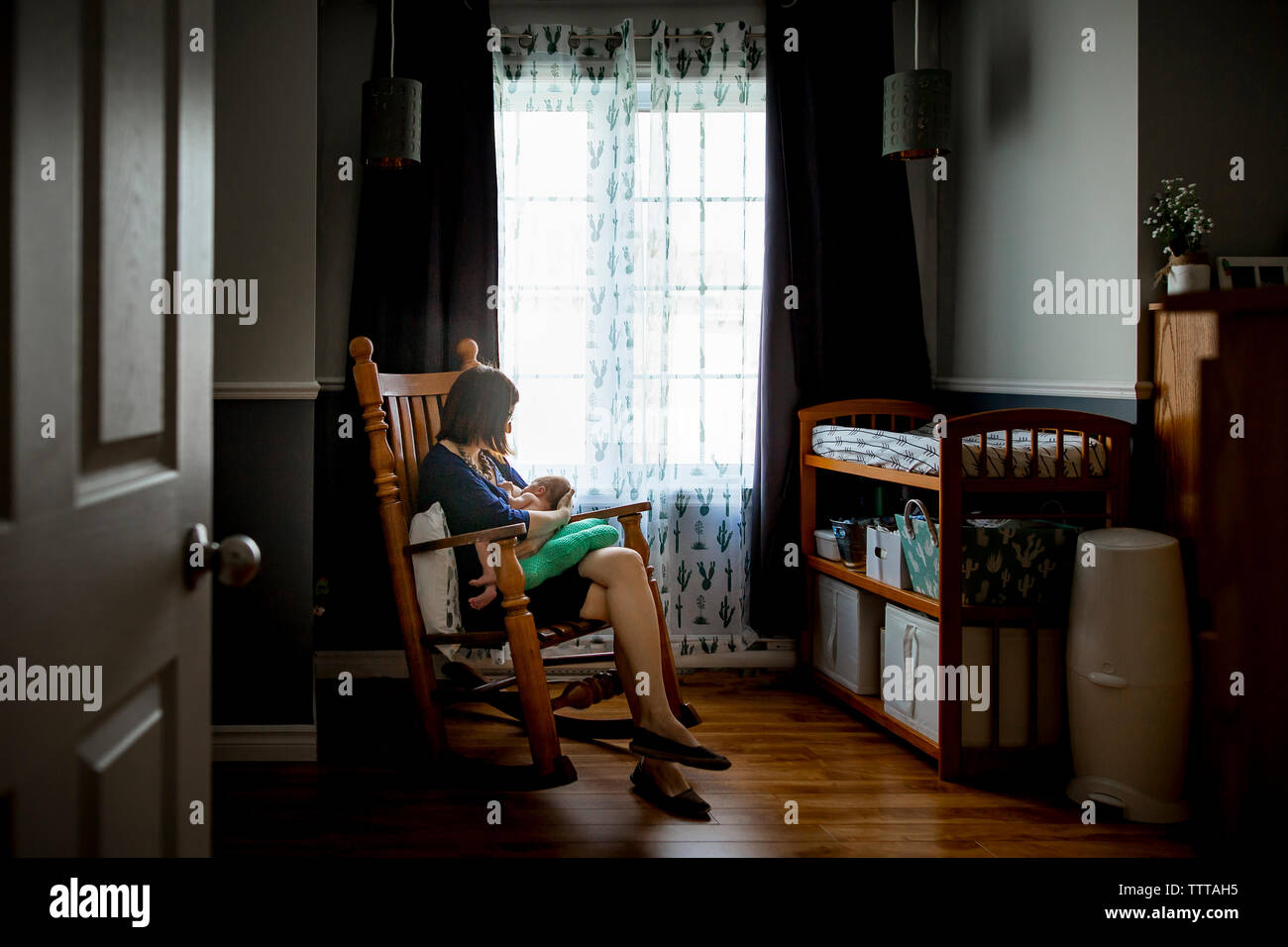 Mother breastfeeding newborn son while sitting on rocking chair seen