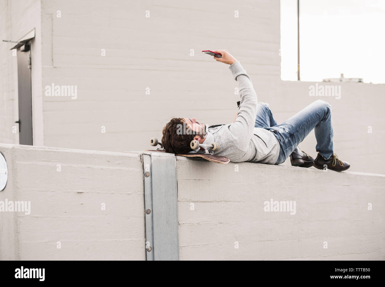 Full length of man taking selfie while lying on retaining wall Stock Photo