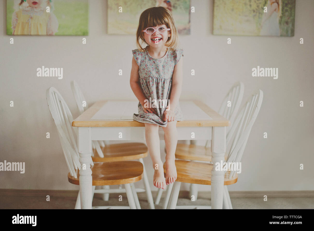 Portrait of cheerful girl sitting on dining table at home Stock Photo