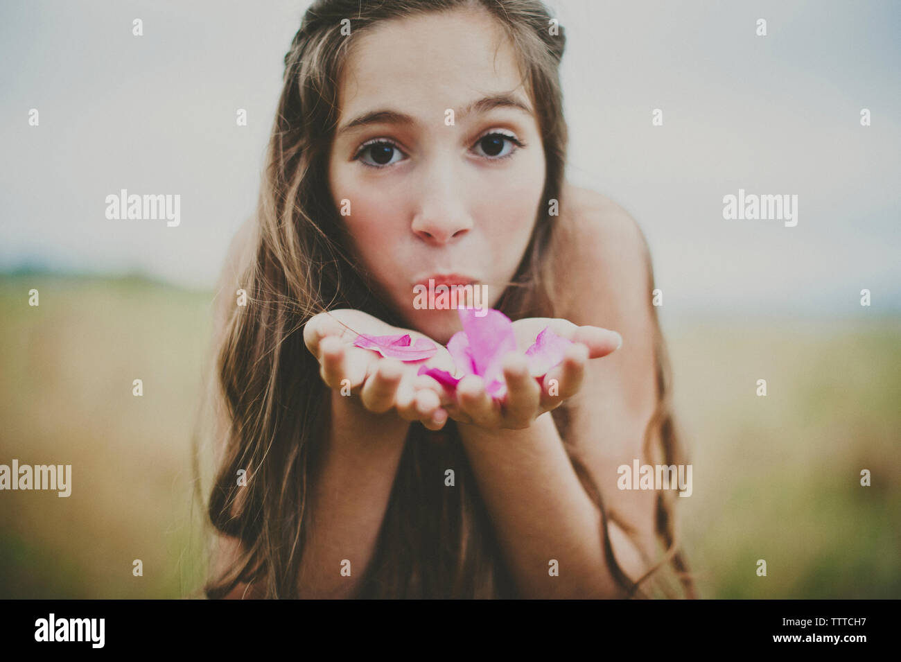 Portrait of happy girl blowing pink flower petals on field Stock Photo