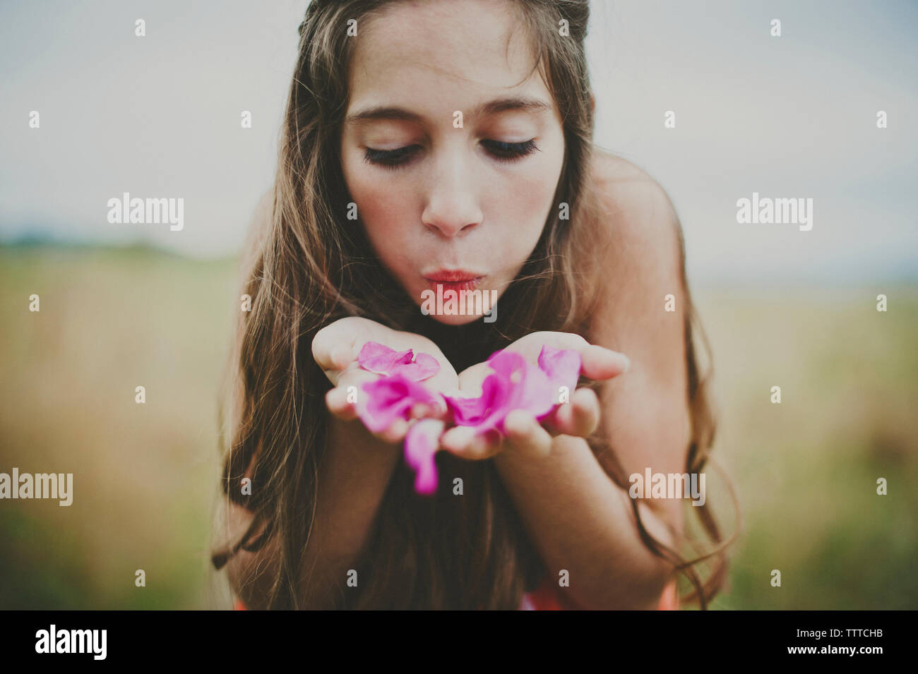 Cute girl blowing pink flower petals on field Stock Photo