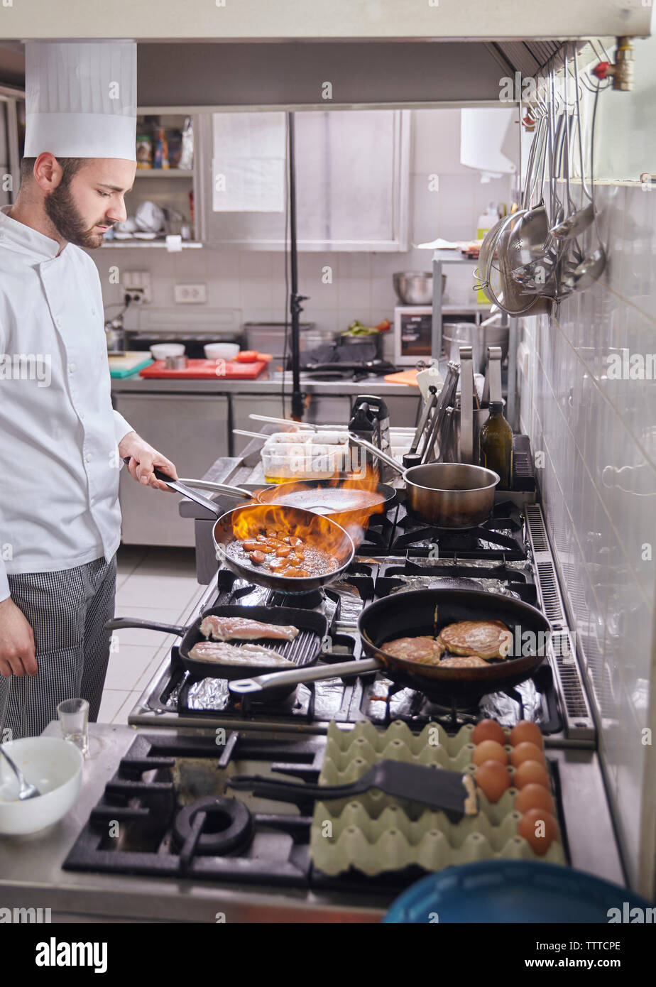 Chef holding flaming pan while preparing food at commercial kitchen Stock Photo