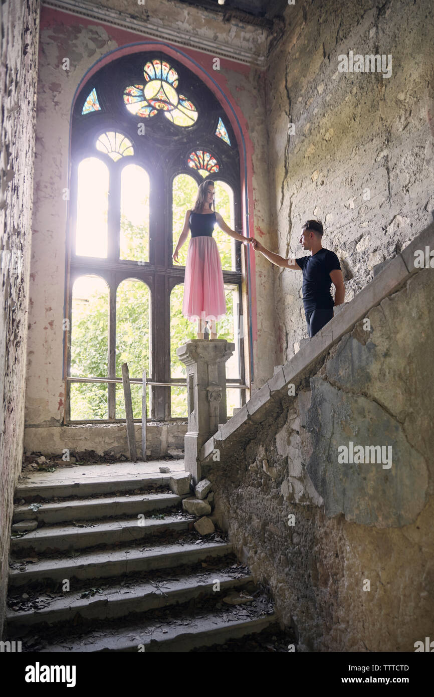 Ballerina standing on newel post while holding male friend's hand in old building Stock Photo