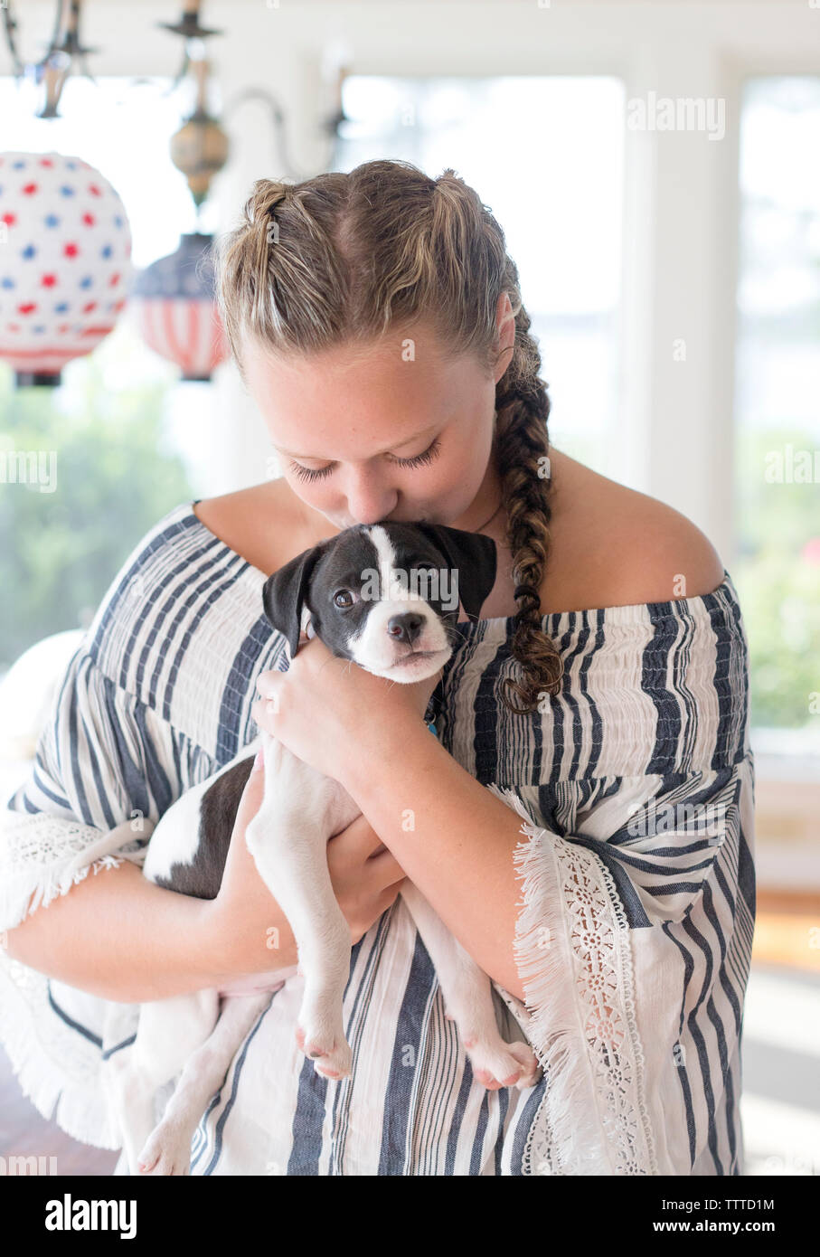 Teen girl with braids holding and kissing a new puppy indoors in Virgi Stock Photo
