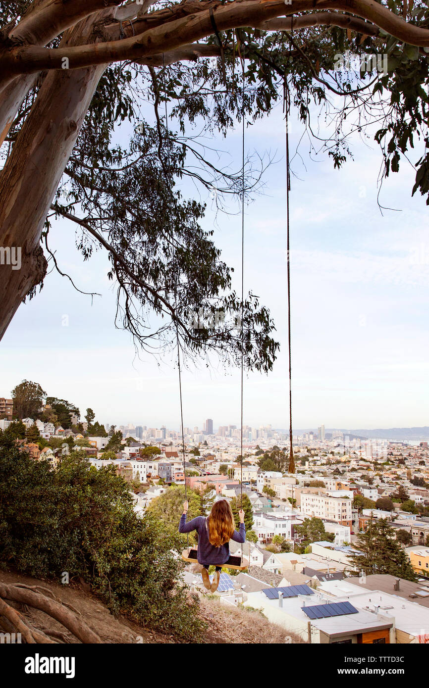 Woman swinging from branch with cityscape in background Stock Photo - Alamy