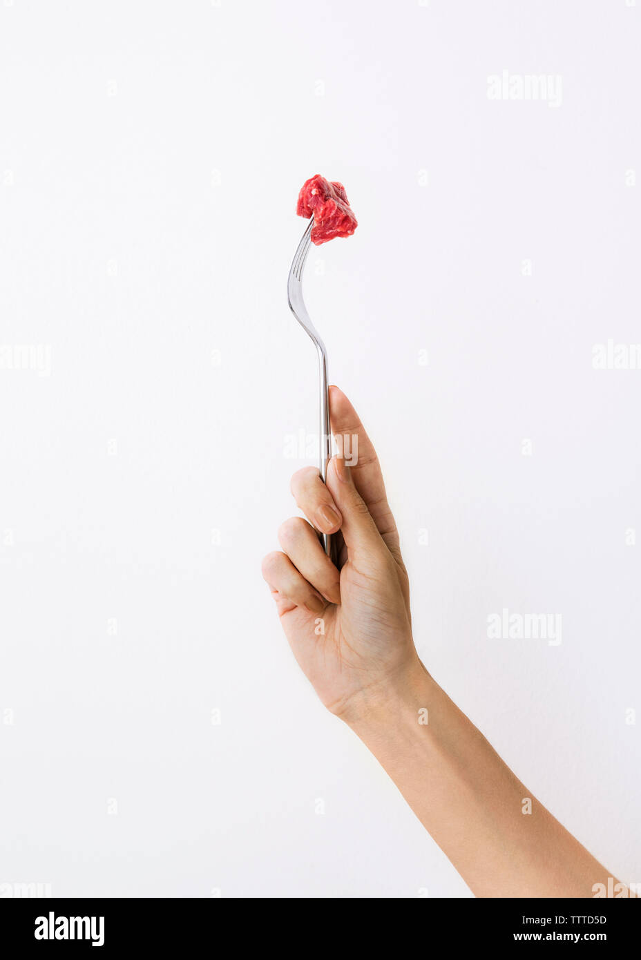 Cropped image of woman holding fork with meat against white background Stock Photo