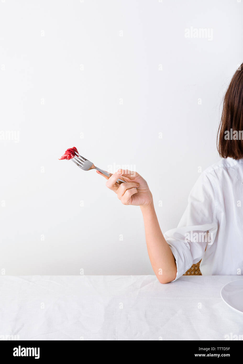 Woman holding fork with meat against white wall Stock Photo