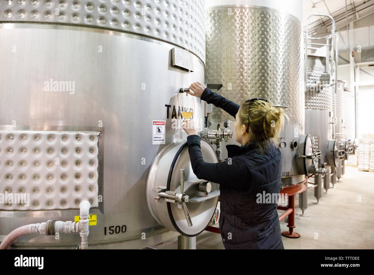 Rear view of female expert tasting wine from industrial tanks Stock