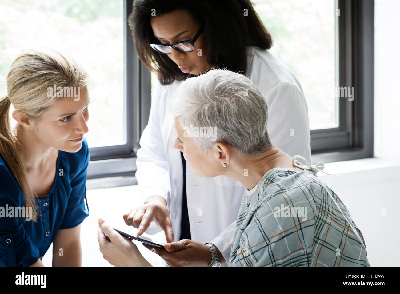 Doctor using tablet while mature female patient looking at daughter in clinic Stock Photo