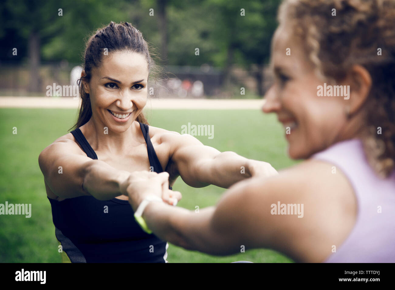 Sportswomen holding hands while stretching at park Stock Photo