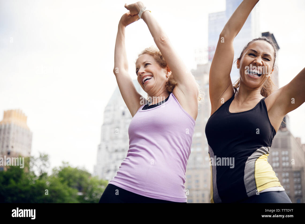 Happy female friends with arms raised stretching in park Stock Photo