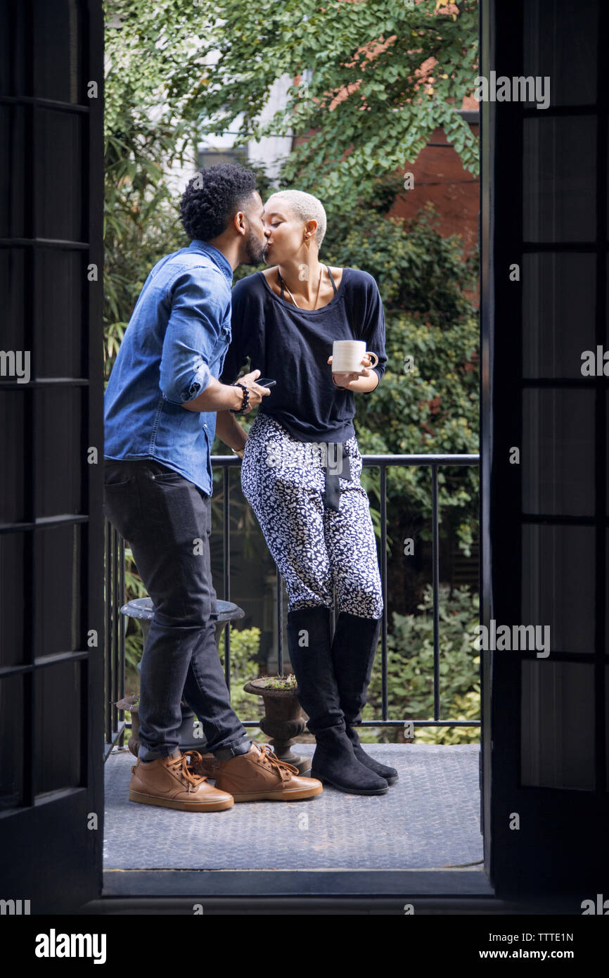 Romantic couple kissing while standing in balcony seen through doorway Stock Photo