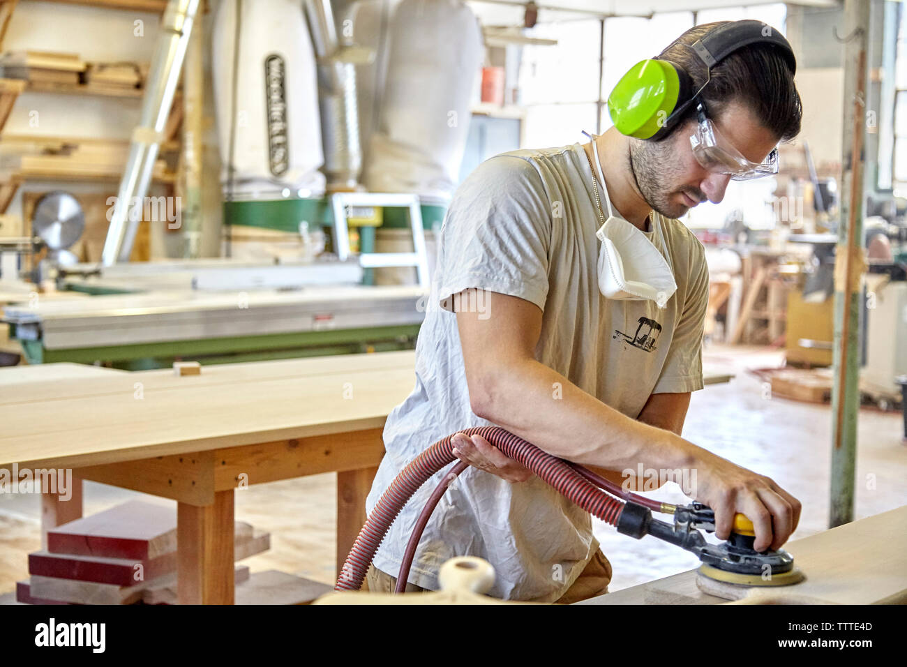 Carpenter using ear and eye protection while sanding wooden plank in workshop Stock Photo