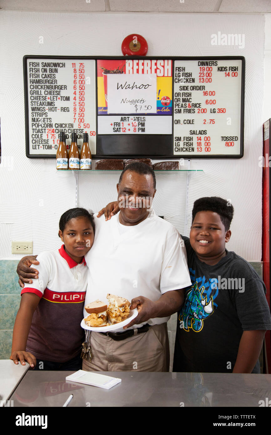 BERMUDA. St. George. Art Mel and  his kids Jade and AJ in his restaurant called Art Me's Spicy Dicy. He is holding his famous Fish Sandwich. Stock Photo