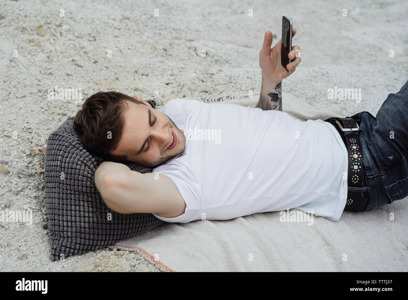 Smiling young man holding smart phone while lying on blanket at beach Stock Photo