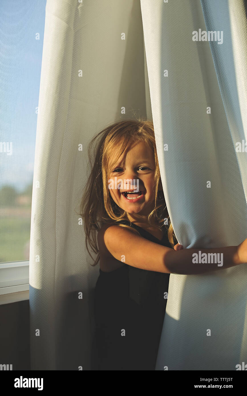 Happy toddler amuses herself by playing, unplugged, in curtains. Stock Photo