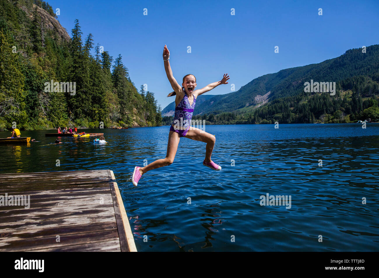 Front view of girl jumping into the lake surrounded by moutains Stock Photo