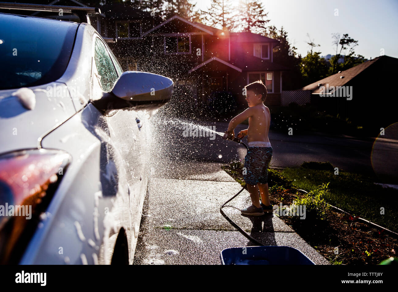 side view of boy washing car with hose Stock Photo