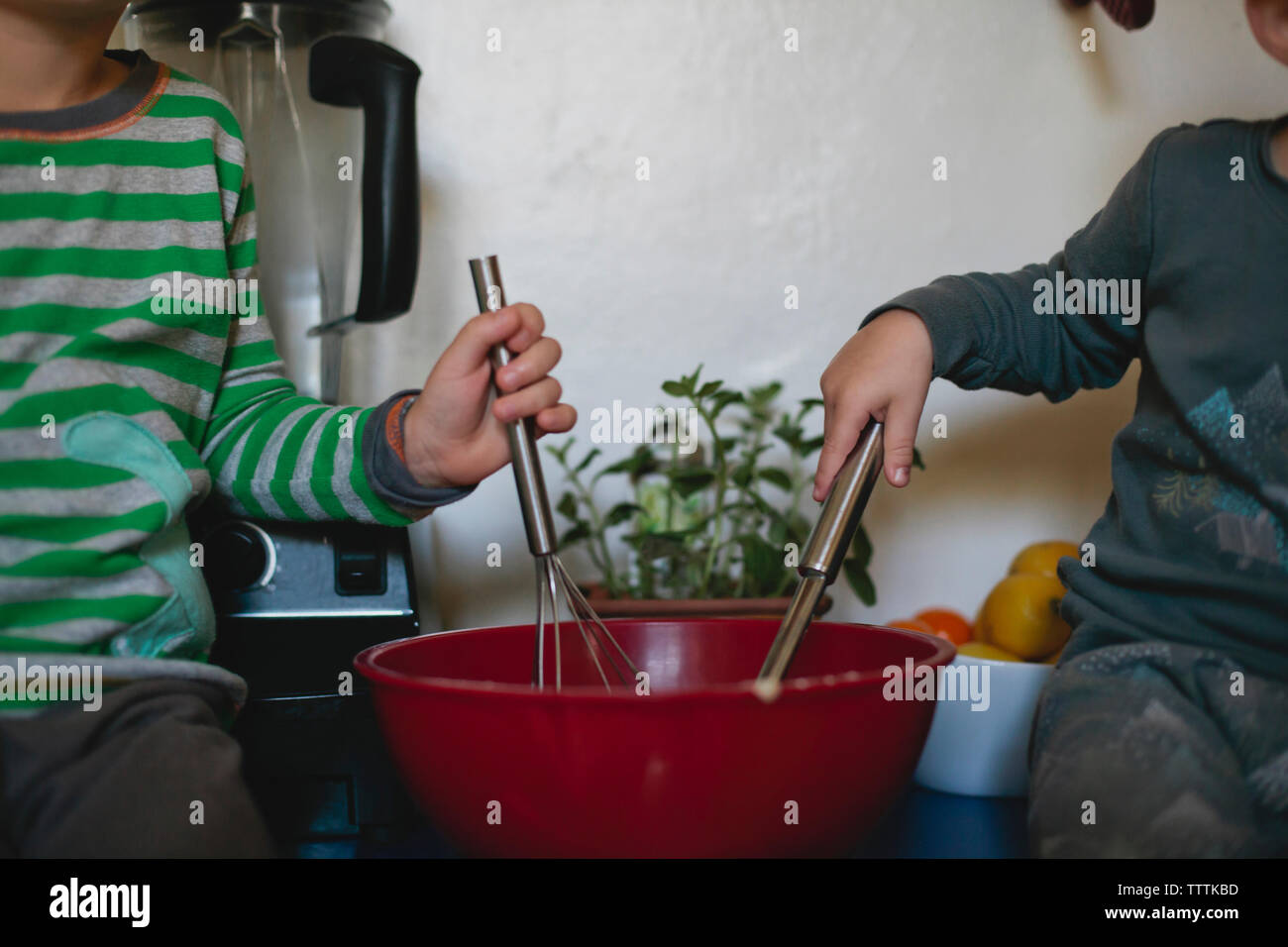 Midsection of brothers whisking while sitting on kitchen counter Stock Photo