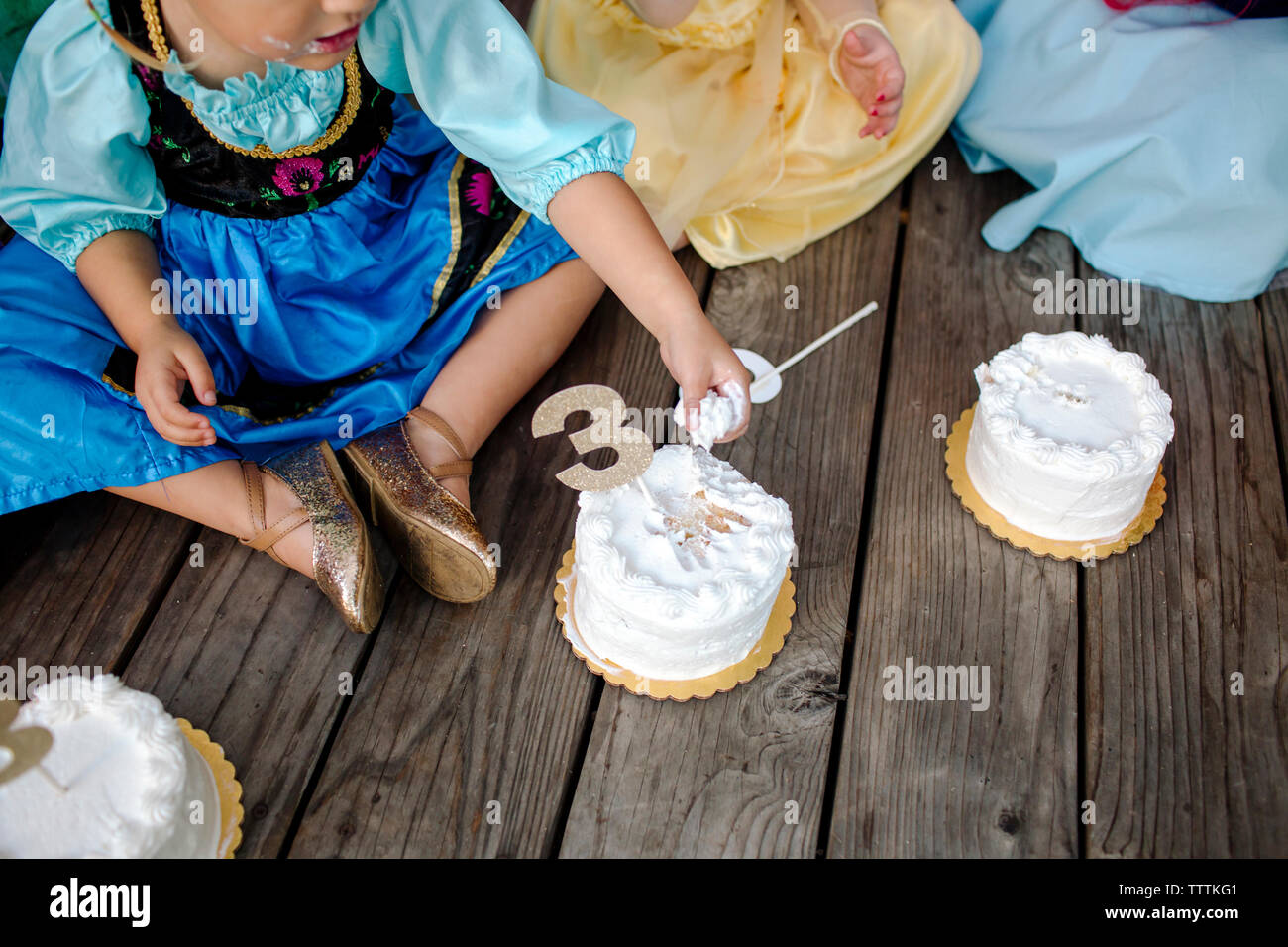 High angle view of girls having cakes while sitting on floorboard during princess party Stock Photo