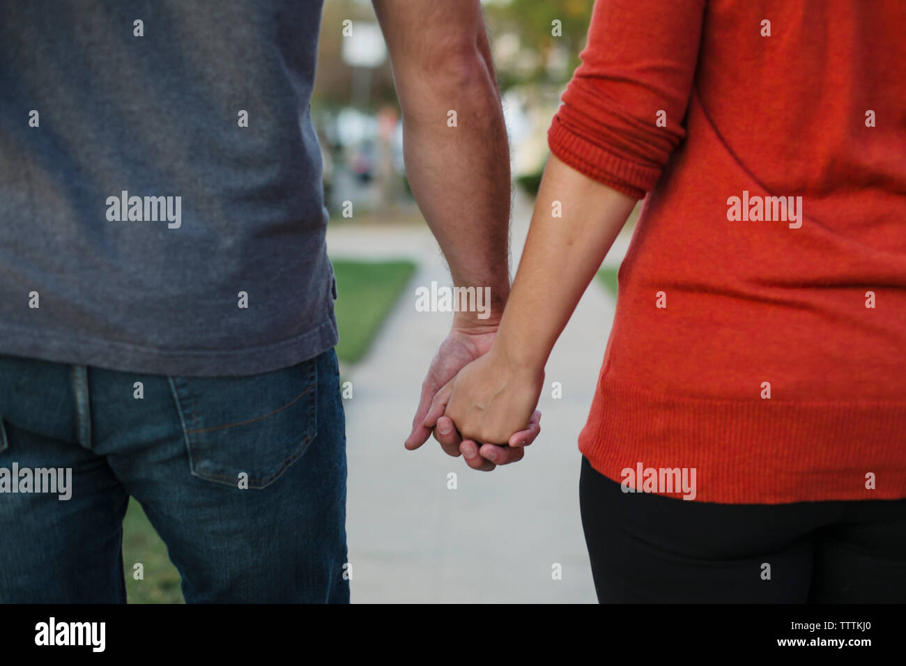Midsection of couple holding hands while standing at lawn Stock Photo