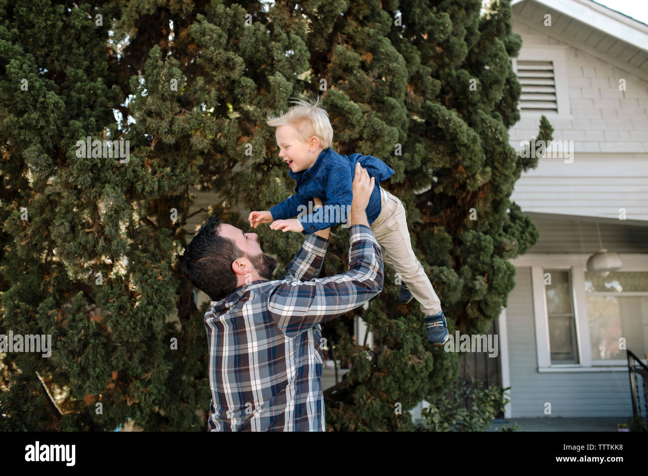 Father picking up son while standing by tree at backyard Stock Photo