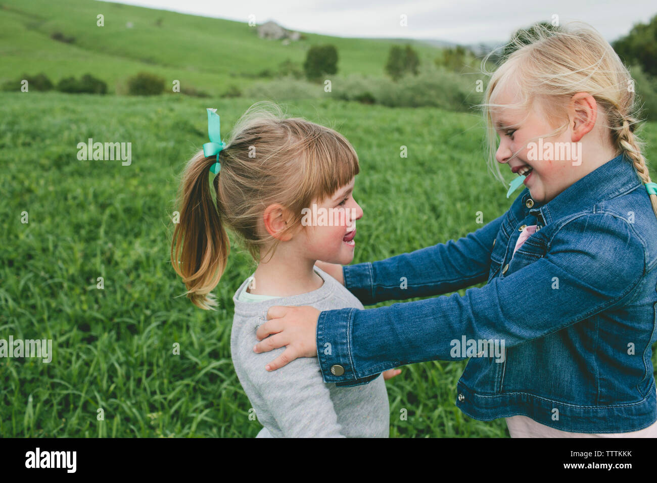 Side view of happy sisters looking at each other while standing on grassy field Stock Photo