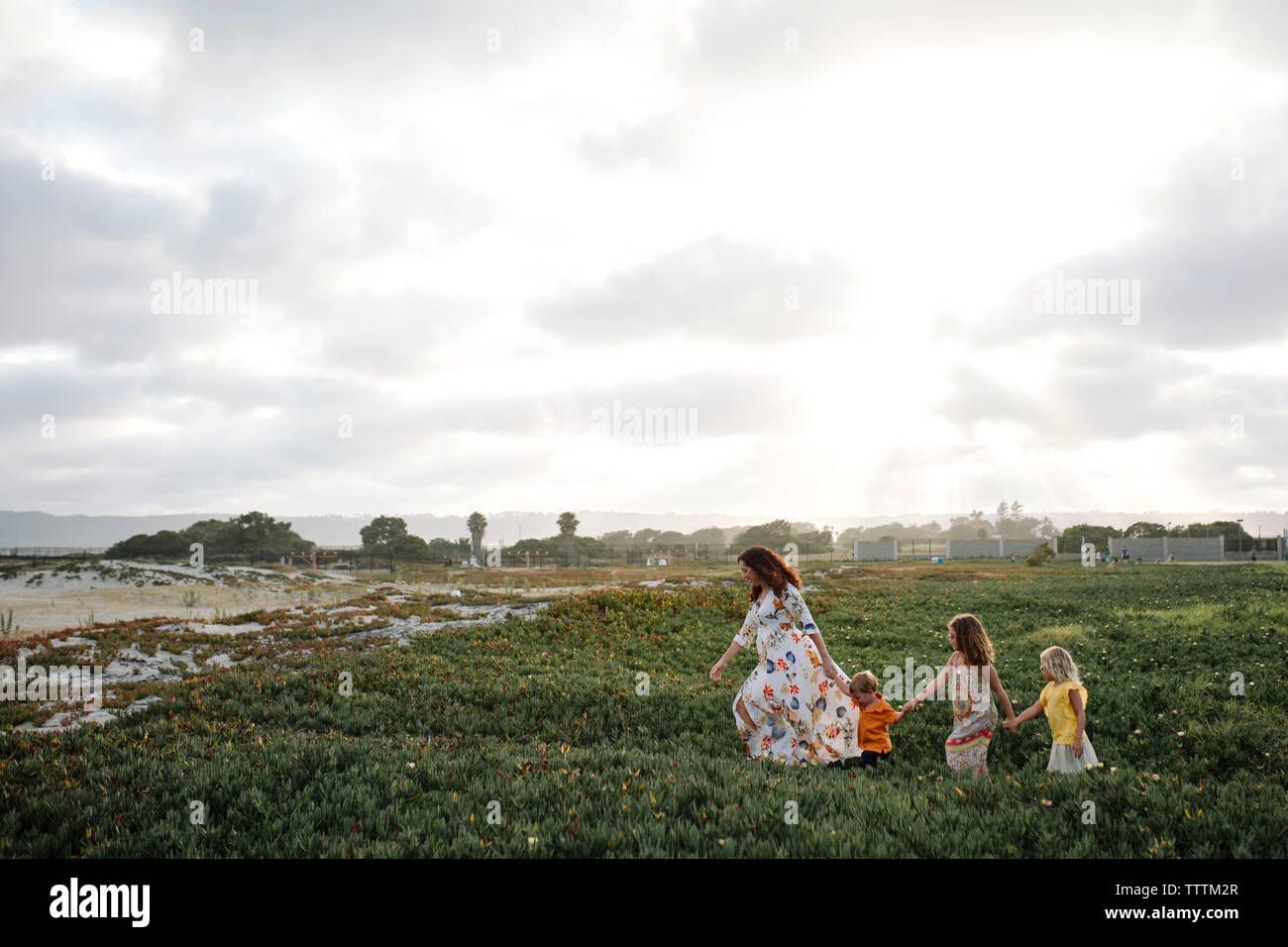 High angle view of mother and children holding hands while walking on field against cloudy sky Stock Photo