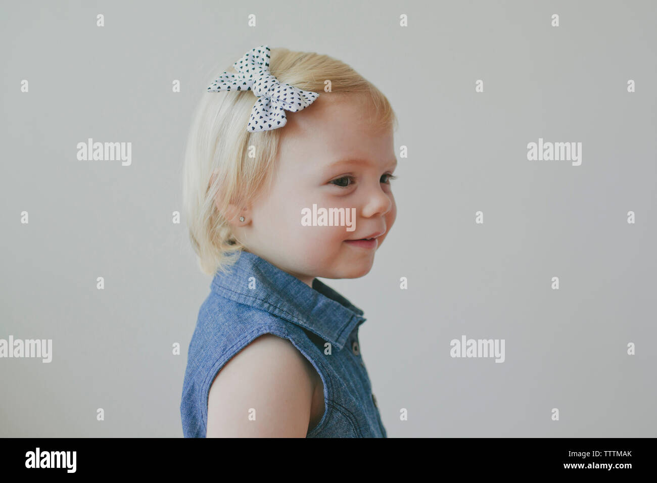 Side view of cute girl wearing bow on her hair against gray background Stock Photo