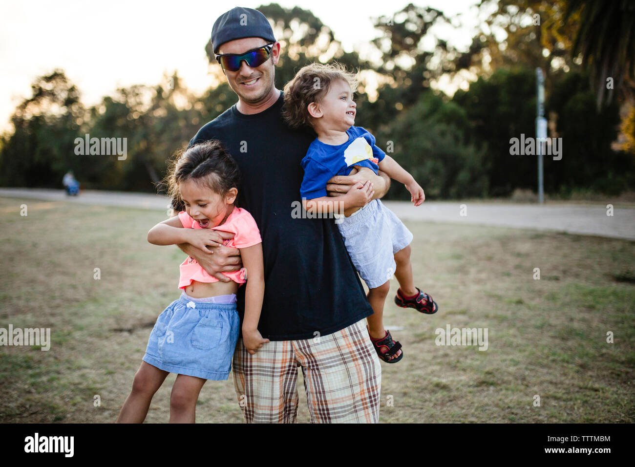 Portrait of playful father carrying daughters at park Stock Photo - Alamy