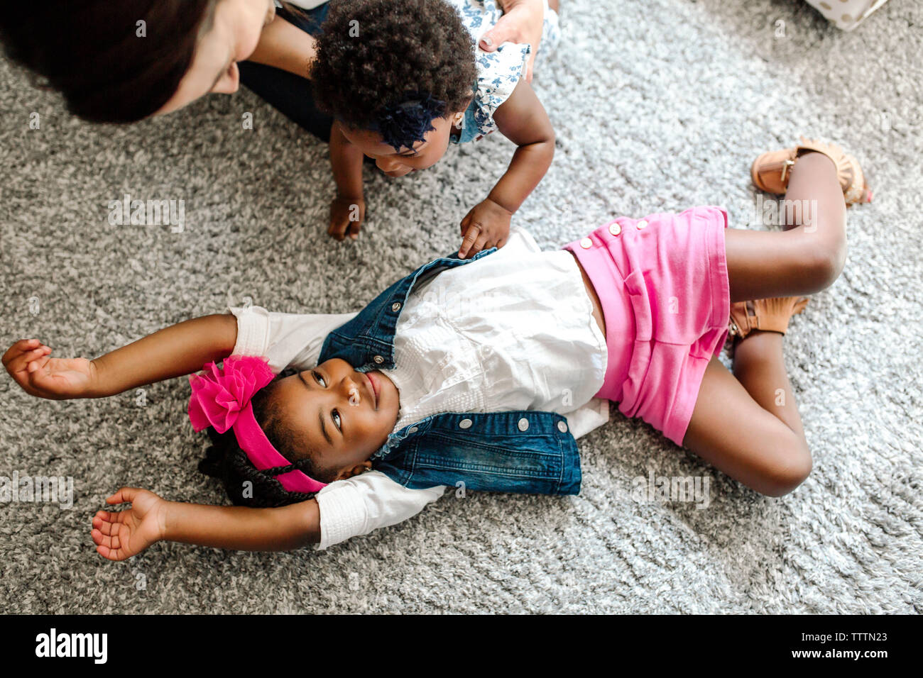 High angle view of mother with daughter looking at girl lying on rug at home Stock Photo