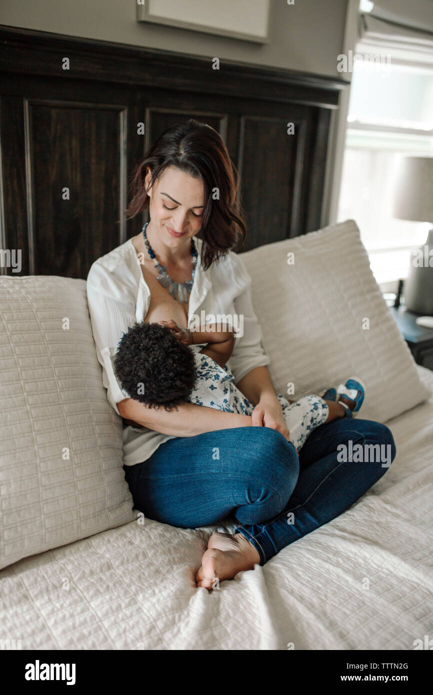 Mother breastfeeding daughter while sitting on sofa at home Stock Photo