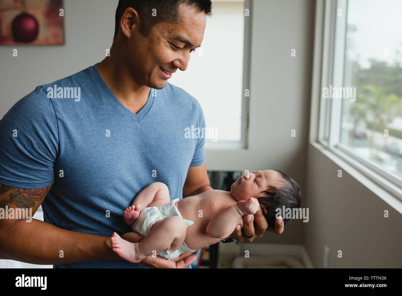 Father carrying shirtless newborn daughter while standing by window at home Stock Photo